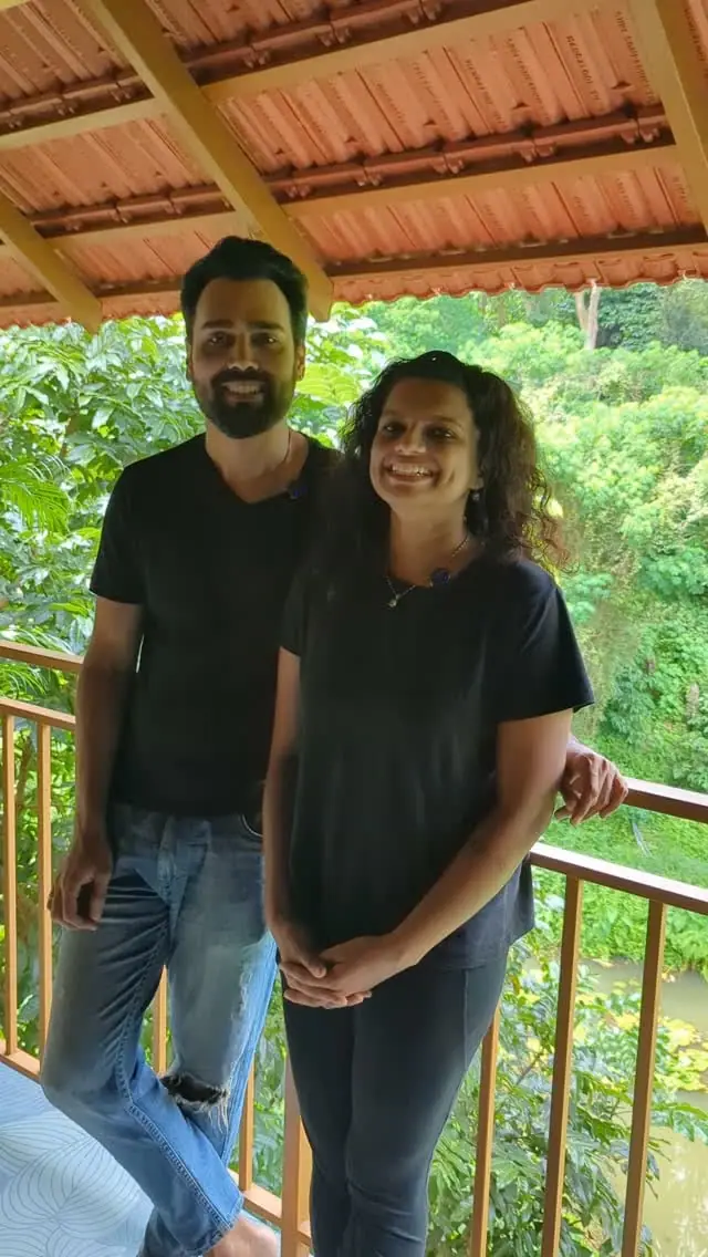 A guest couple on a balcony with greenery and water behind them