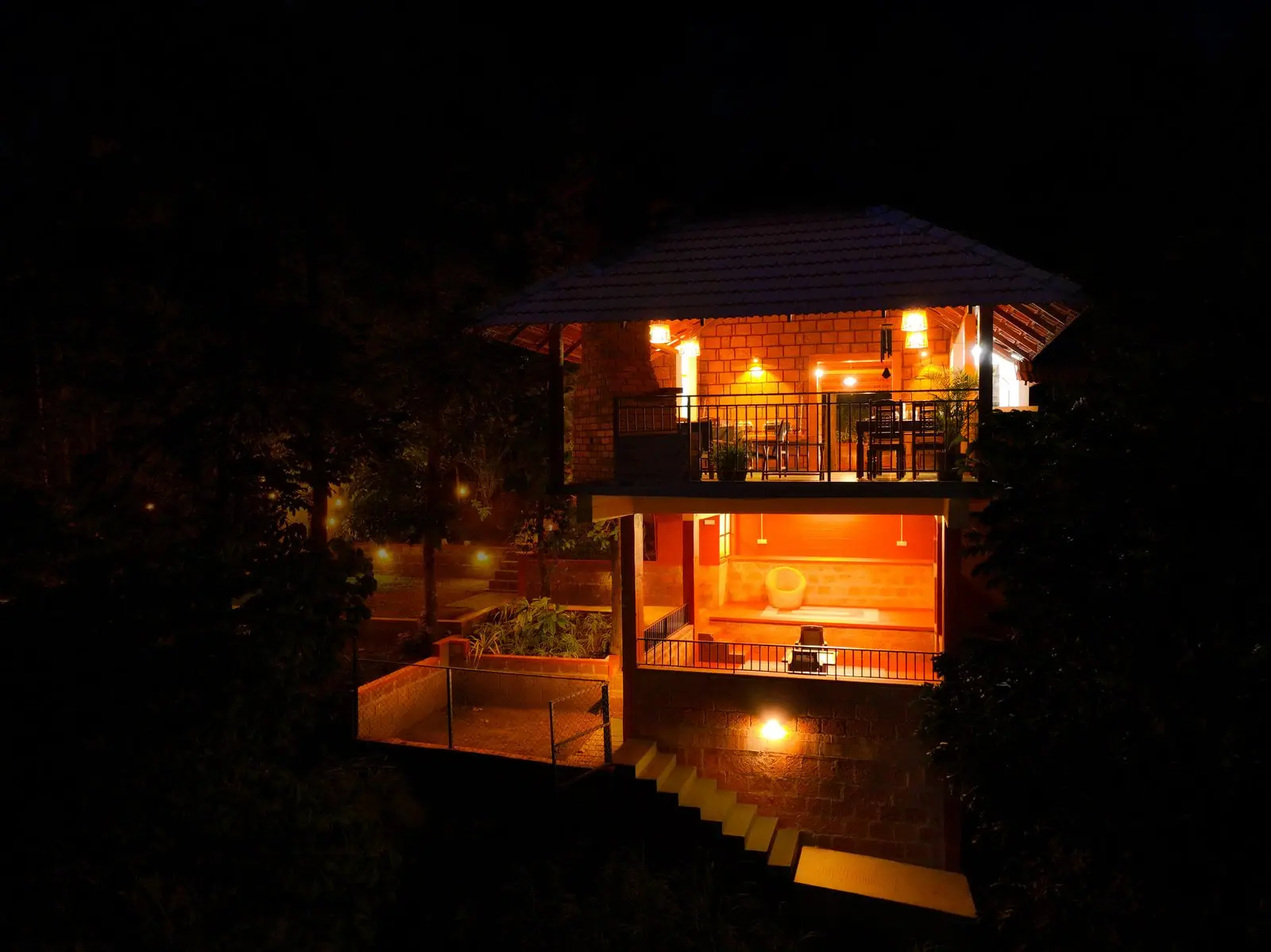 Drone view of a cottage glowing with lamplight among dark trees