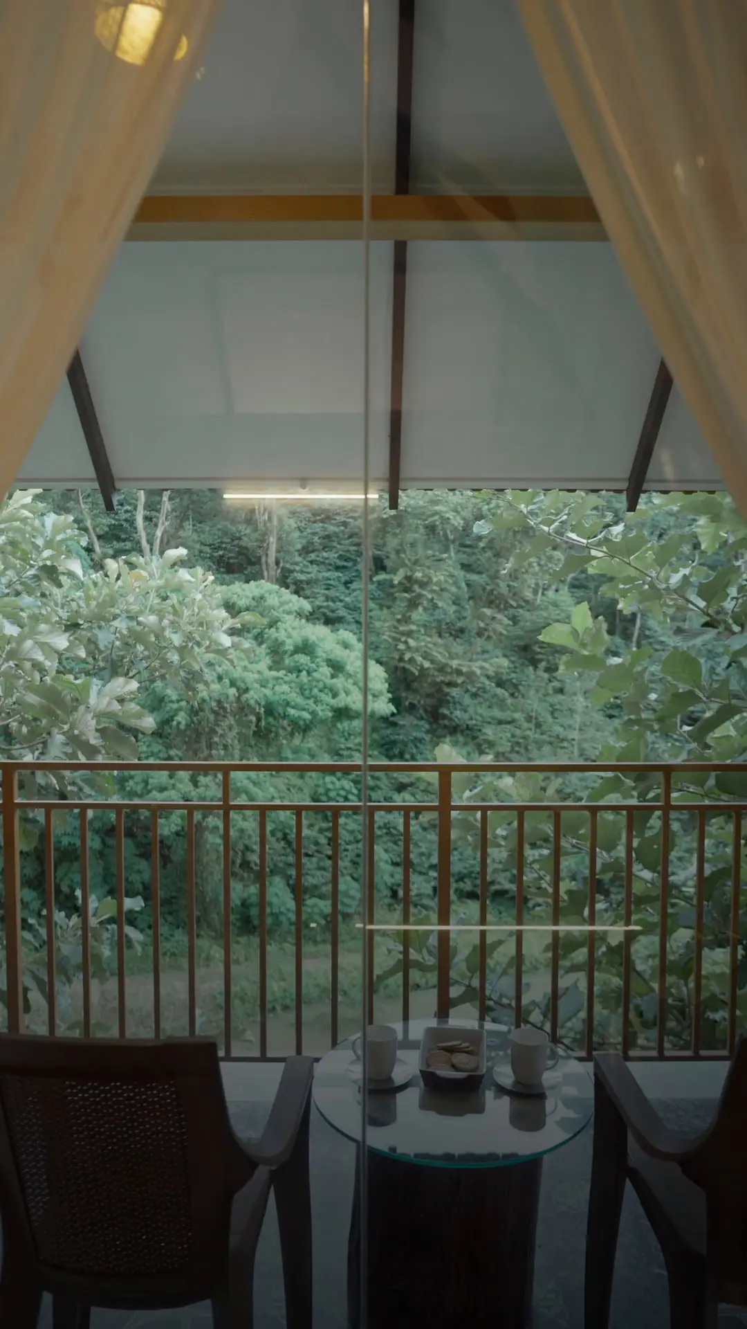 Curtains open from the suite onto the balcony, the forest right beyond the rail
