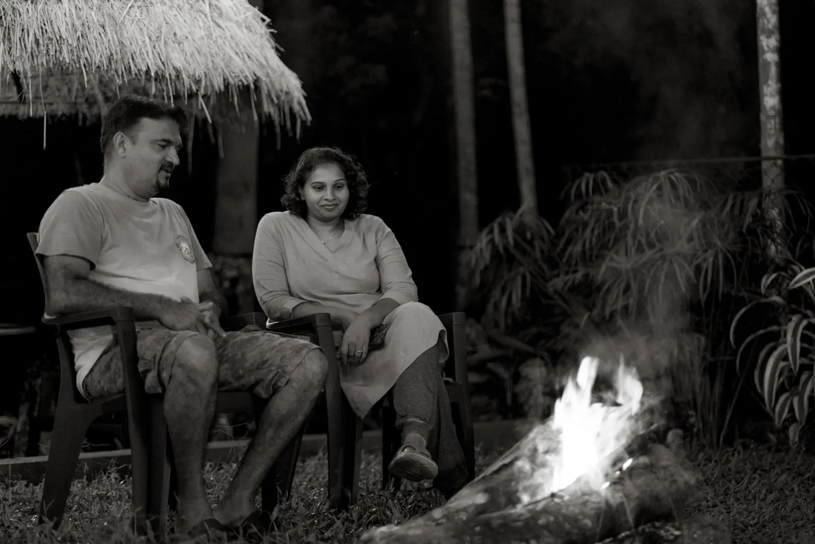 Two people seated by a bonfire at night, in black and white