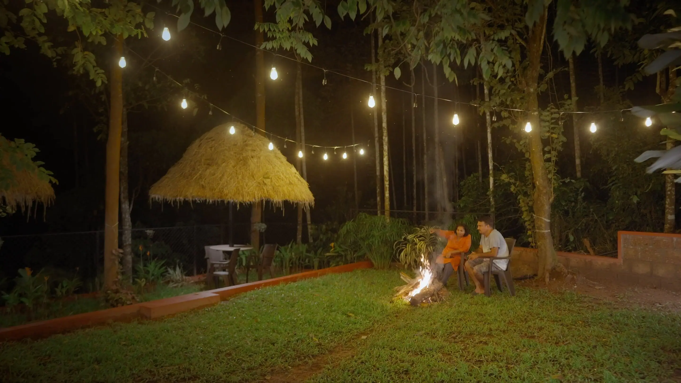 A bonfire on the lawn after dark, with string lights in the trees on a coffee estate in South Coorg