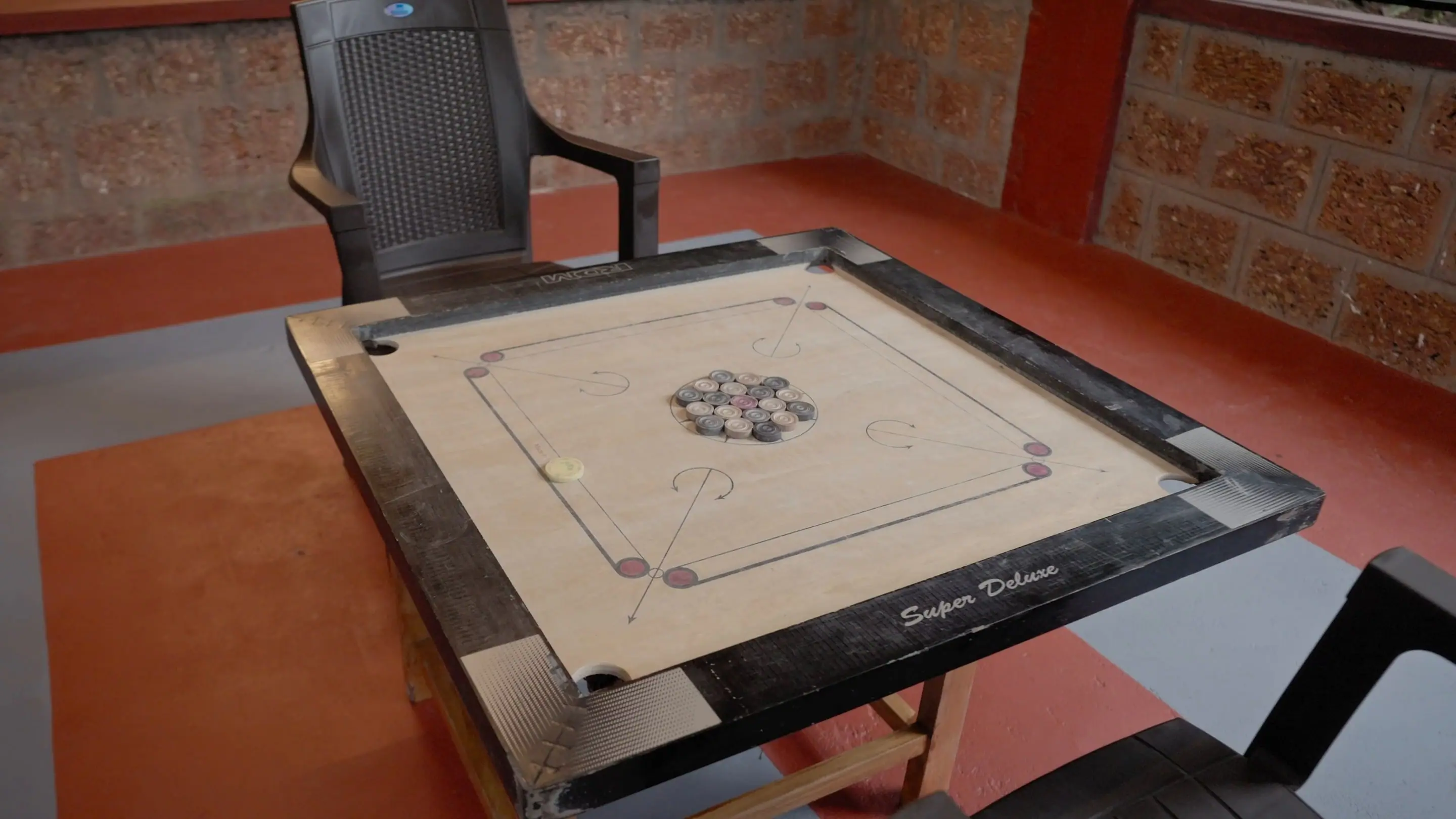 A carrom board set up on the red-floored veranda