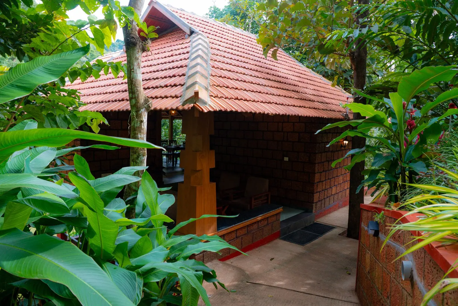 A guest cottage with a clay-tiled roof and laterite walls, framed by banana leaves and garden planting