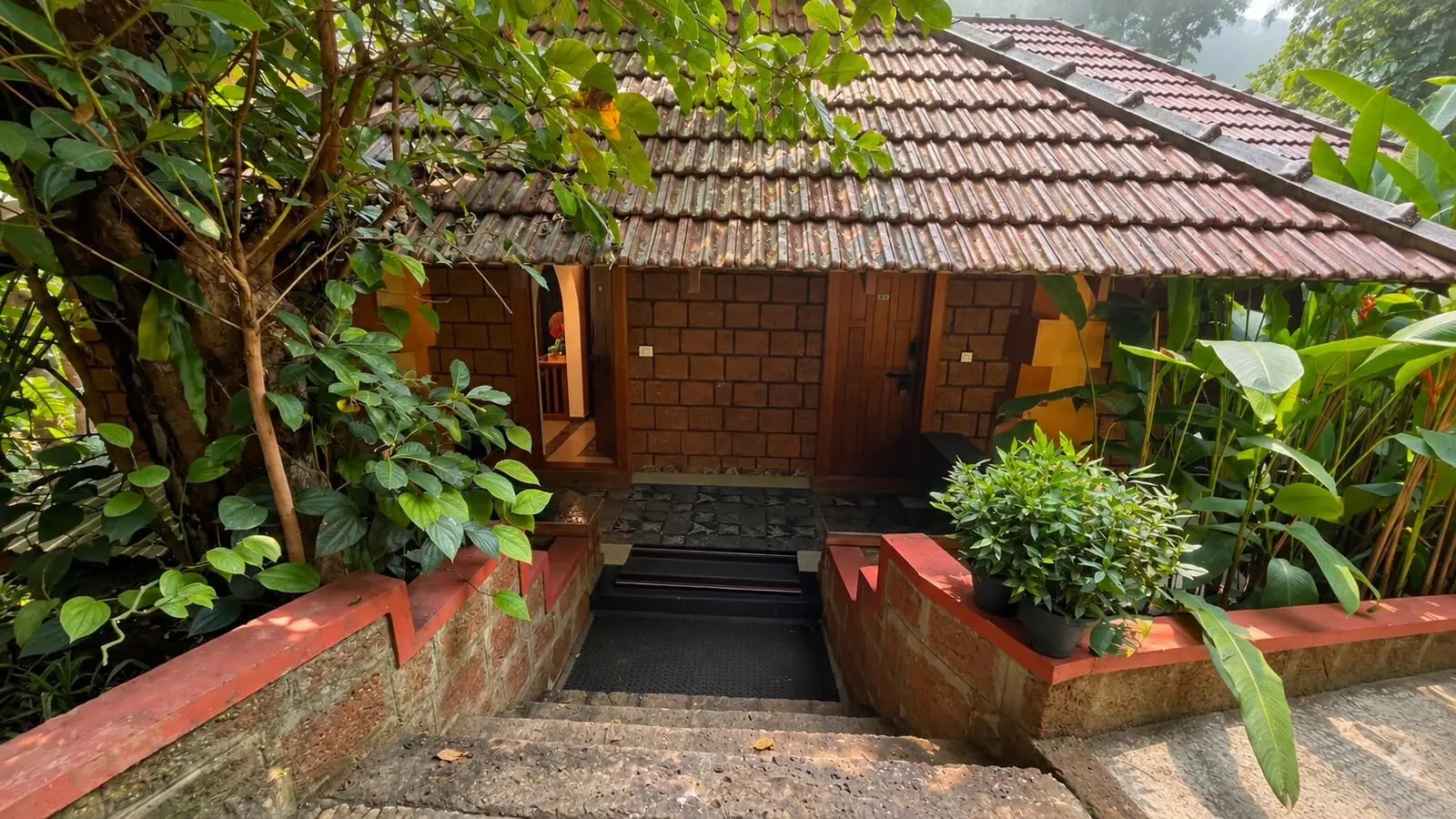 A cottage entrance with a clay-tiled roof and potted plants on laterite planters