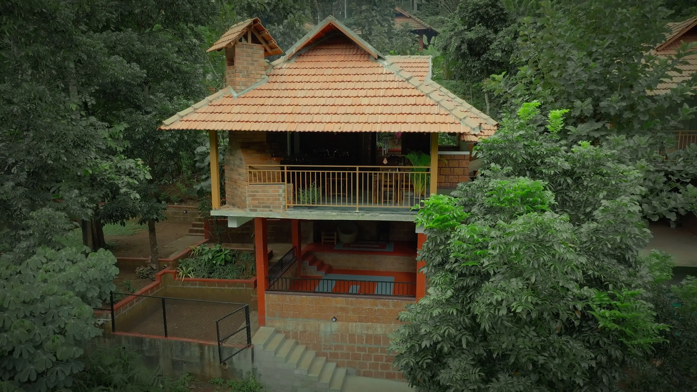 A clay-tiled cottage raised on red posts among the trees and planting of the estate garden