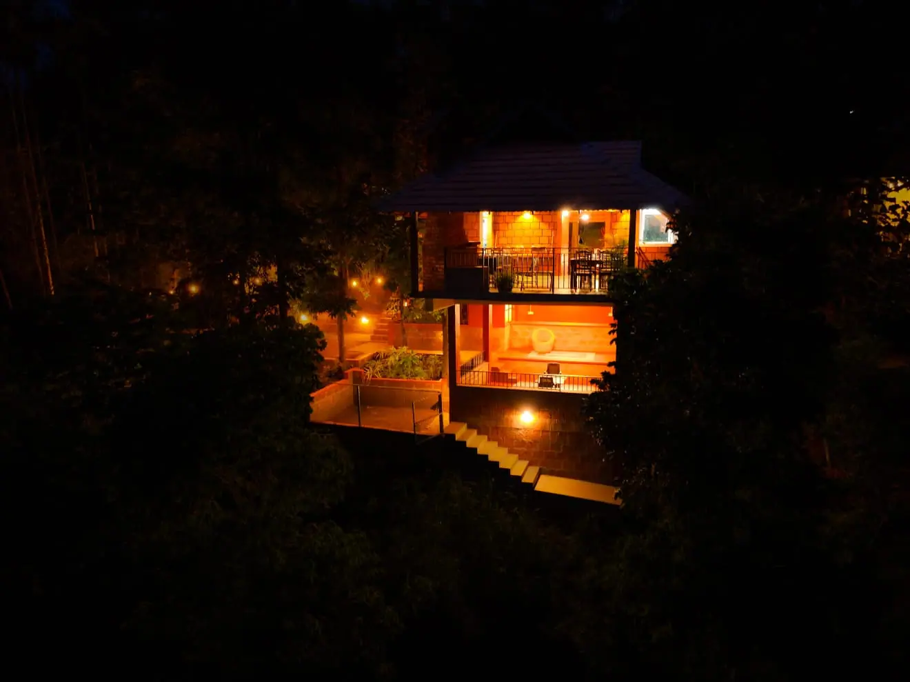 A cottage raised on red posts glowing with warm light among dark trees at night