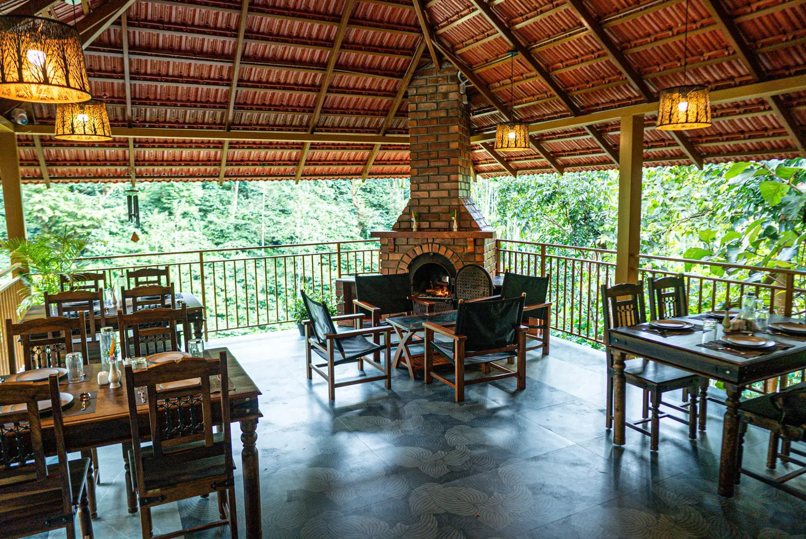 The open dining pavilion with timber tables set around a brick fireplace, the forest beyond the rail