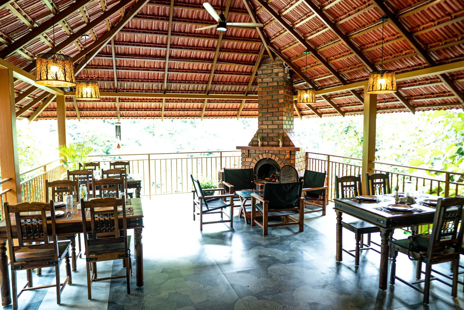 The open dining pavilion with long timber tables, a brick fireplace at one end and the forest beyond