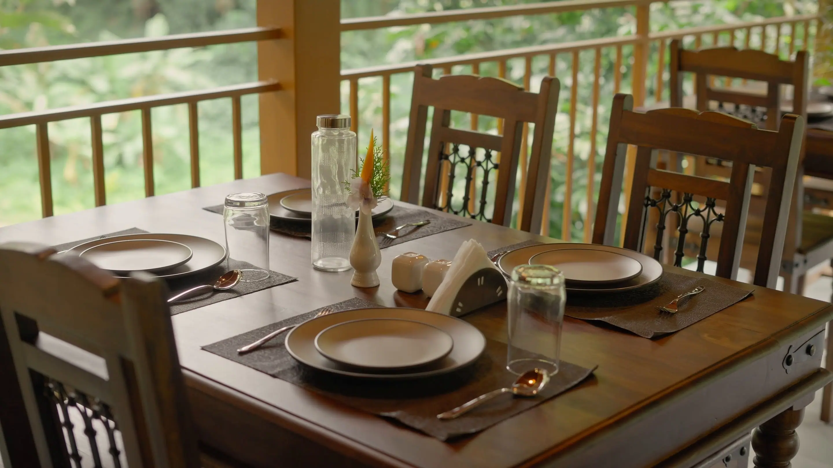 A table laid for breakfast in the open dining pavilion, plates and napkins set, the forest beyond the rail