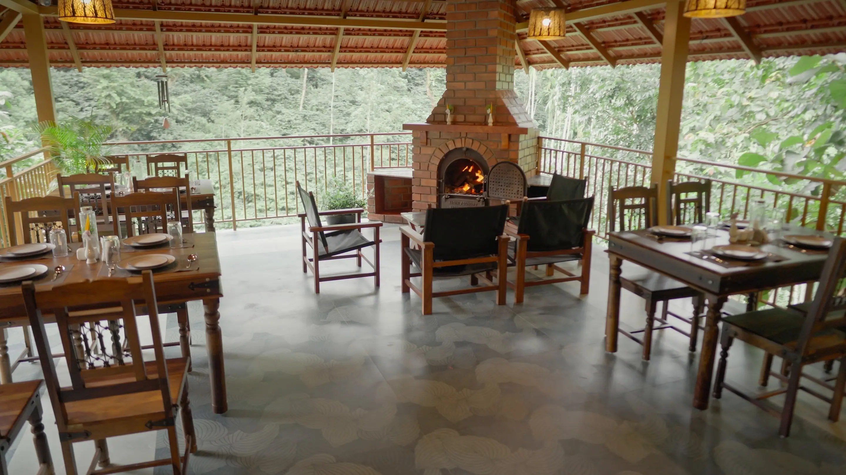 Tables laid in the open dining pavilion, the brick fireplace behind and the forest beyond the rail