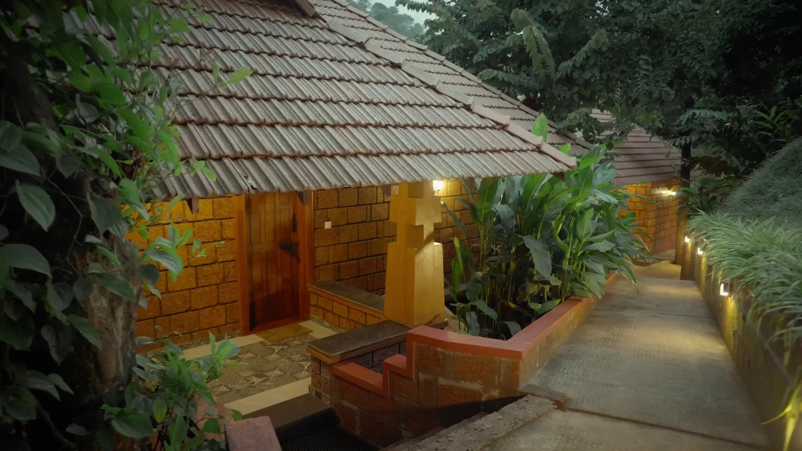 Dusk at Mokha Grove: a lamp-lit path between the laterite cottages