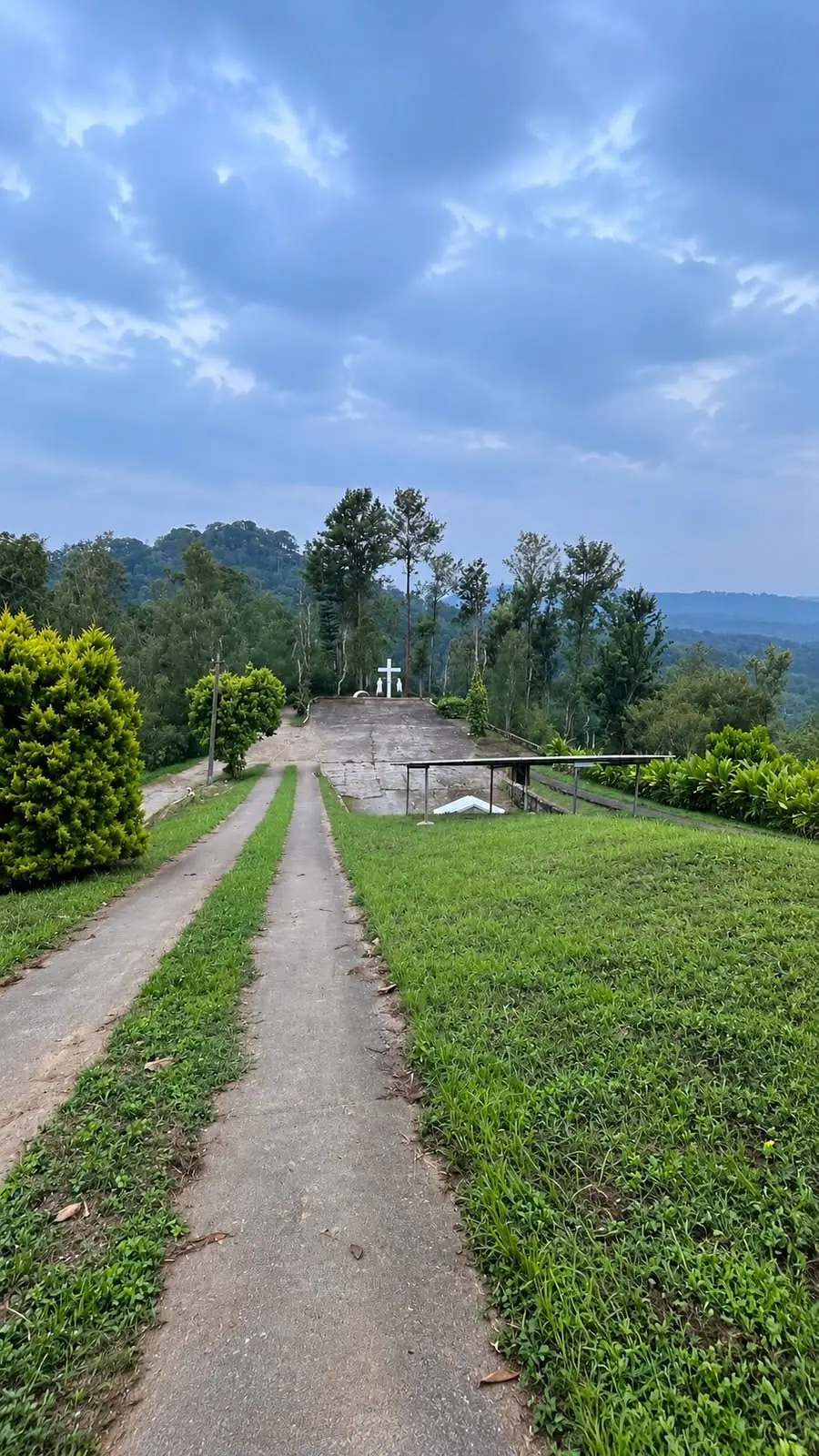 A cross on a hilltop path among trees, near the estate