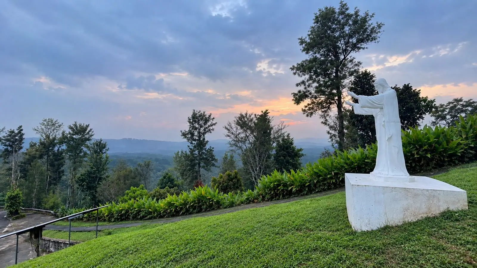 A white statue on a hilltop above a wide, forested valley in South Coorg