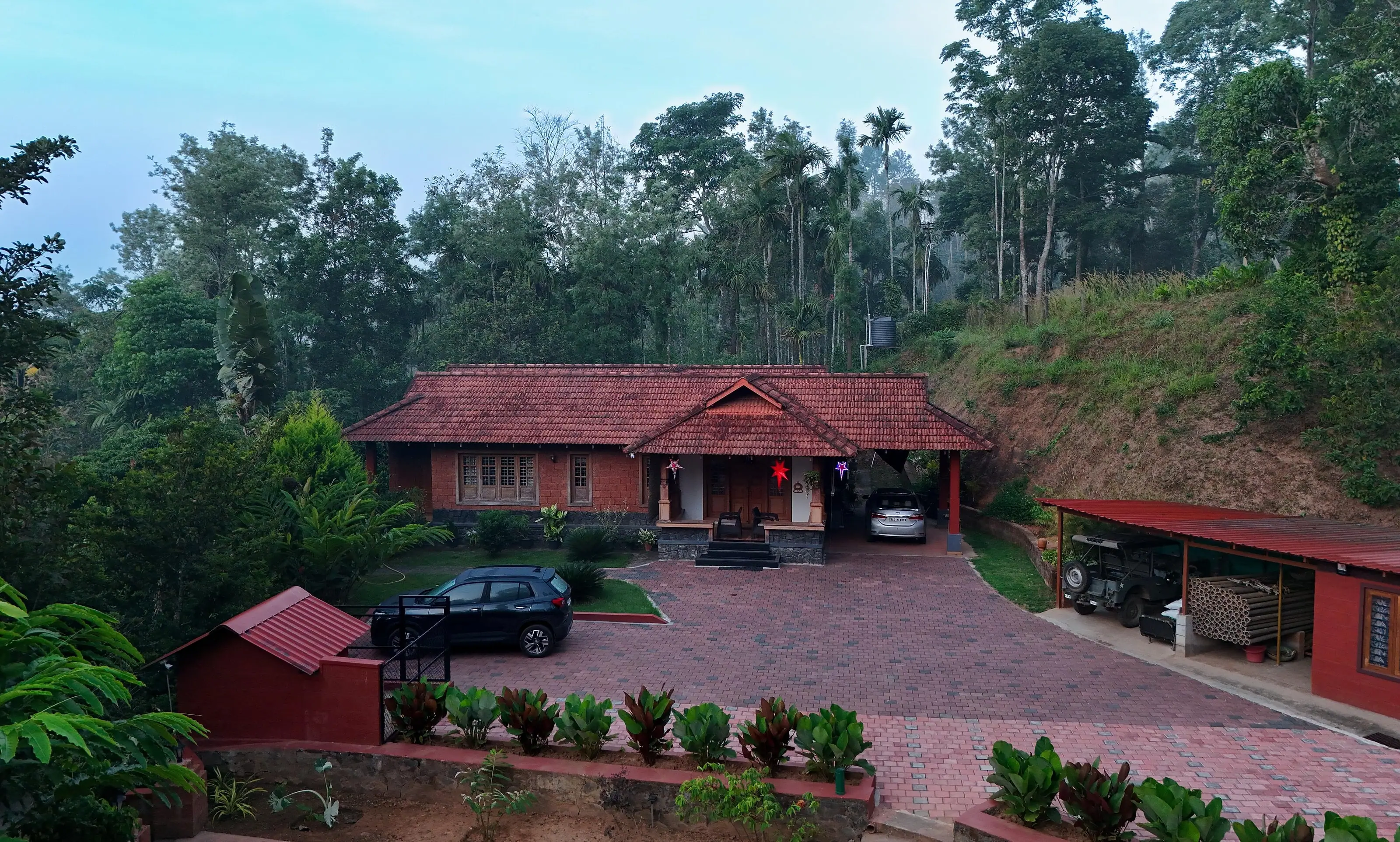 The hosts' home: a clay-tiled house with laterite walls behind a brick-paved courtyard, the estate jeep parked in an open shed on the right