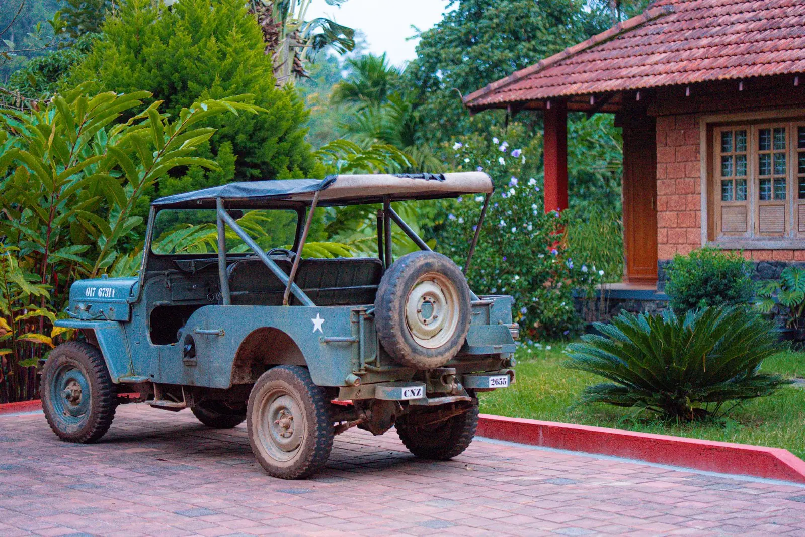 The estate's open jeep parked on a brick drive beside a laterite cottage