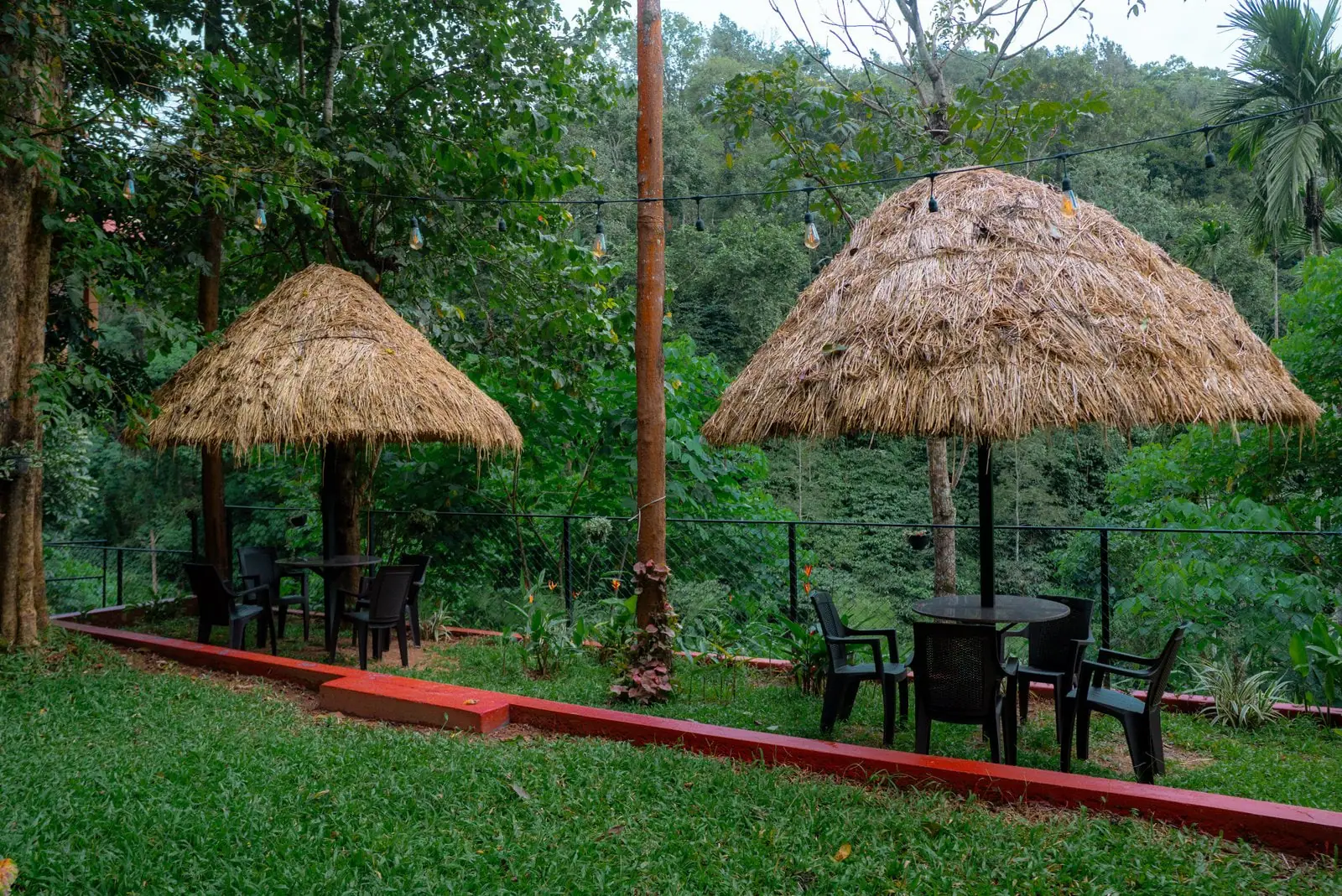 Two thatched gazebos with tables and chairs on the lawn, the forest dropping away behind them
