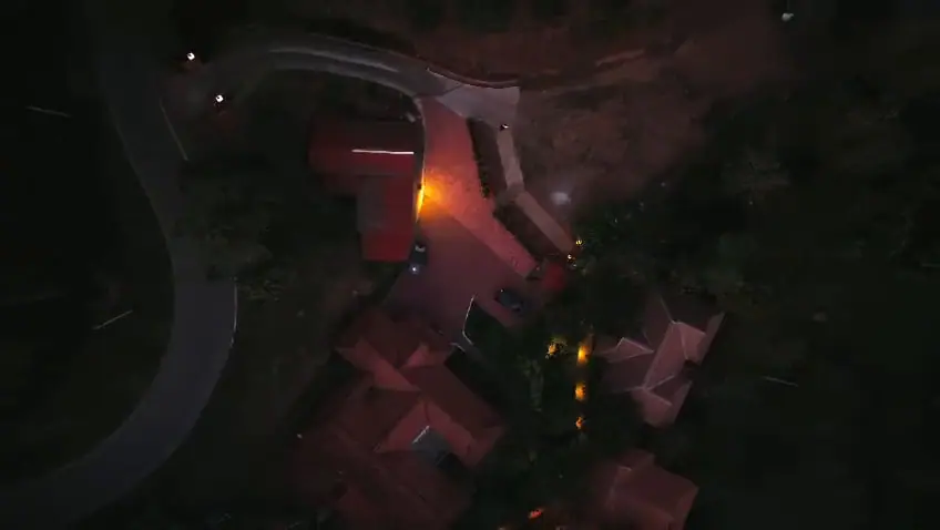 Drone view straight down on Mokha Grove at night: lamplit roofs, garden lights and the road curving past