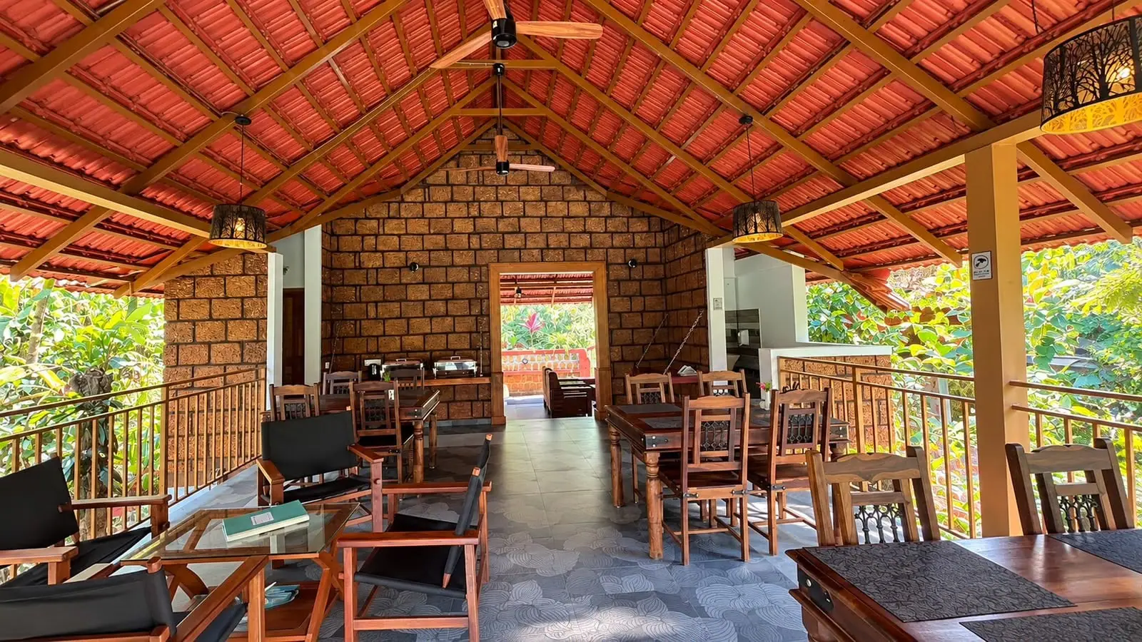 The estate's laterite pavilion under a clay-tiled roof, with timber tables and chairs and green hills beyond