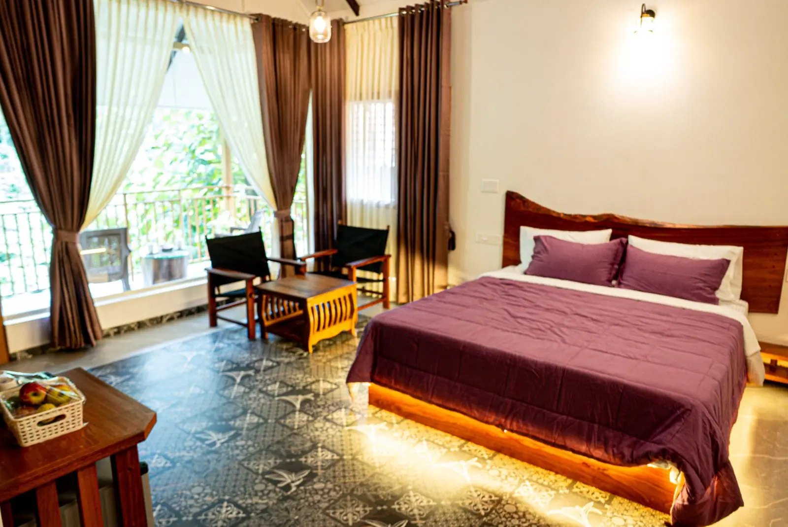 The suite's king bed on an under-lit timber base, the live-edge headboard behind it and the balcony through the curtains