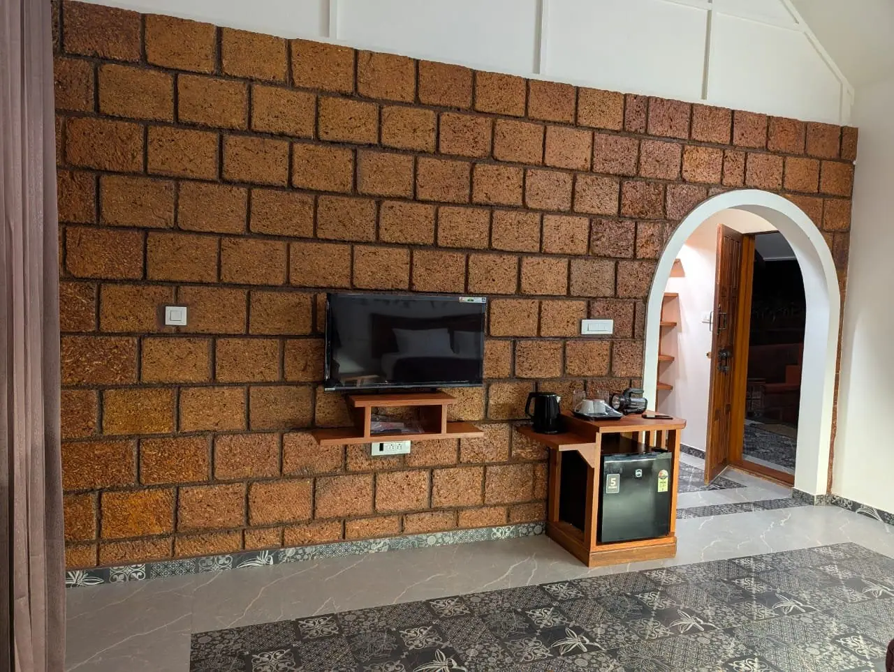 The suite's laterite wall with the TV, the kettle tray on the minibar and an arched doorway