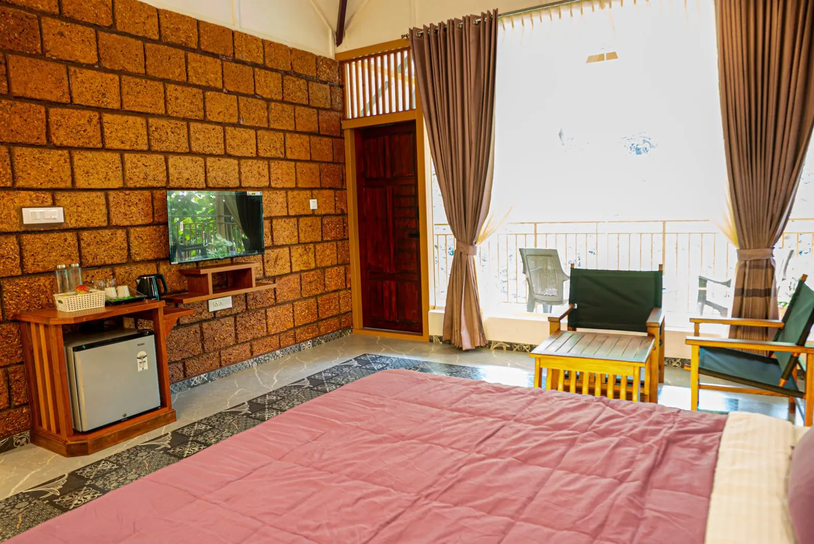 A laterite wall in the suite with the minibar and kettle station, the bed in the foreground
