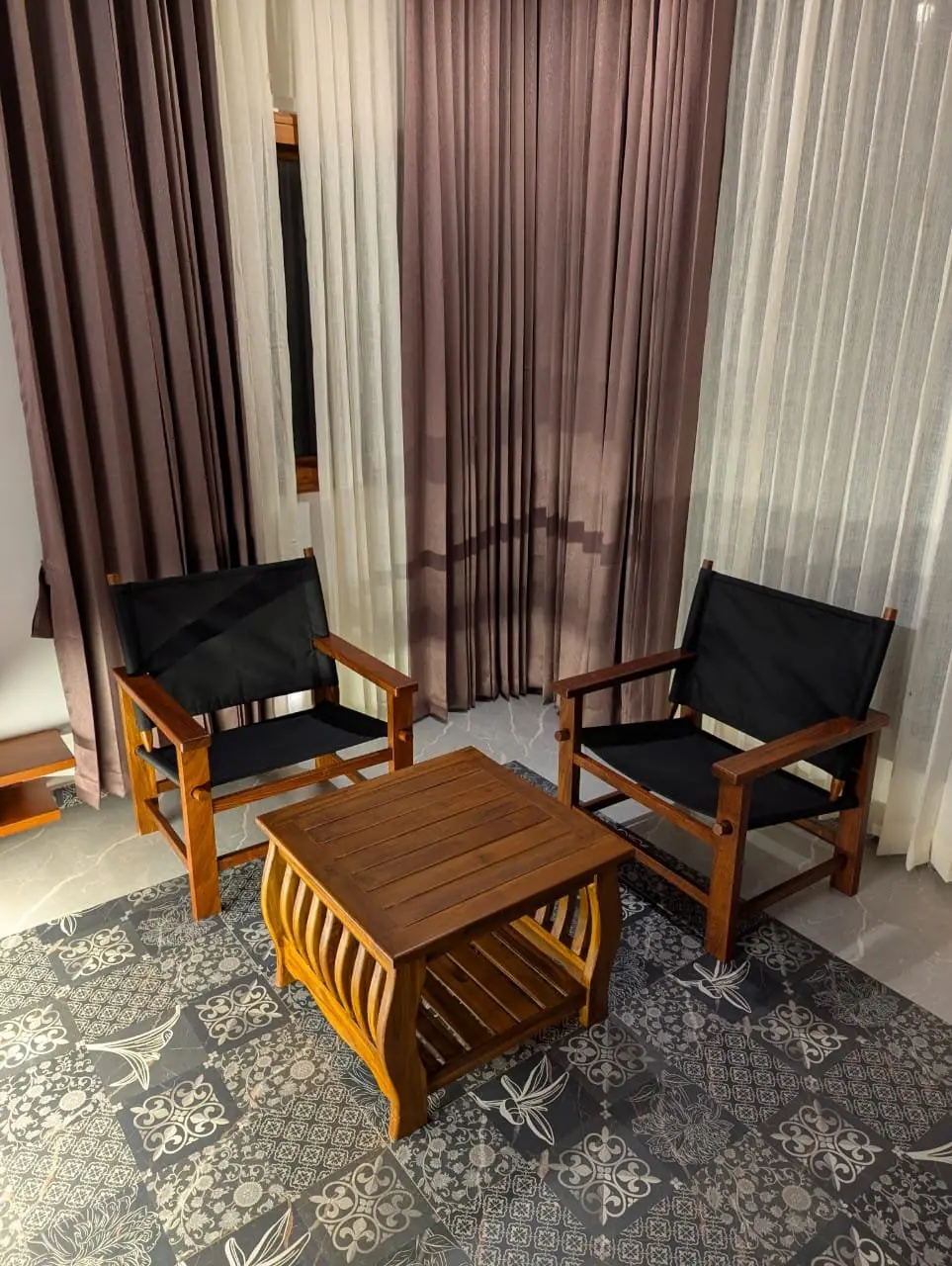 Two timber chairs and a low table by the suite's long curtained windows