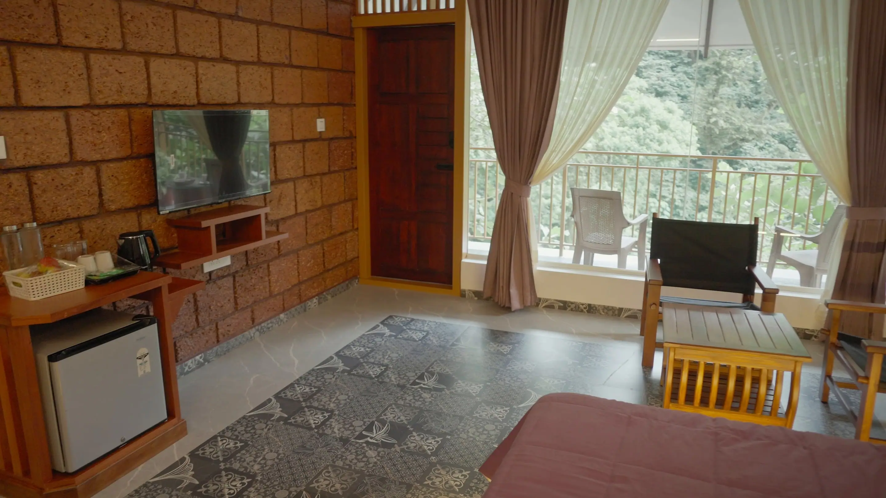 Laterite wall with the TV, kettle station and minibar, the balcony door beyond