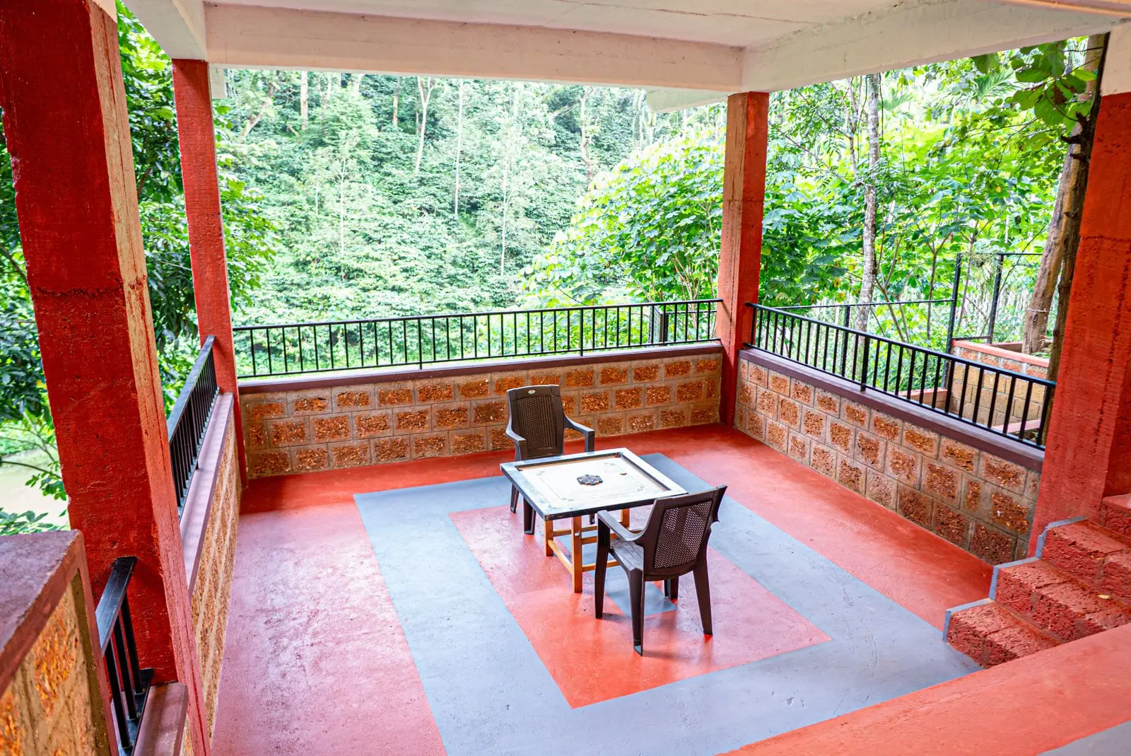 The open veranda with a small table and chairs on its red floor, looking out over the railing to the coffee and trees