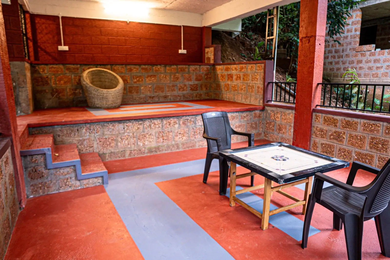 The red-floored veranda with chairs, trees beyond the railing